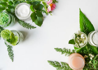 Plant-based skincare ingredients in jars sitting on a table surrounded by greenery.