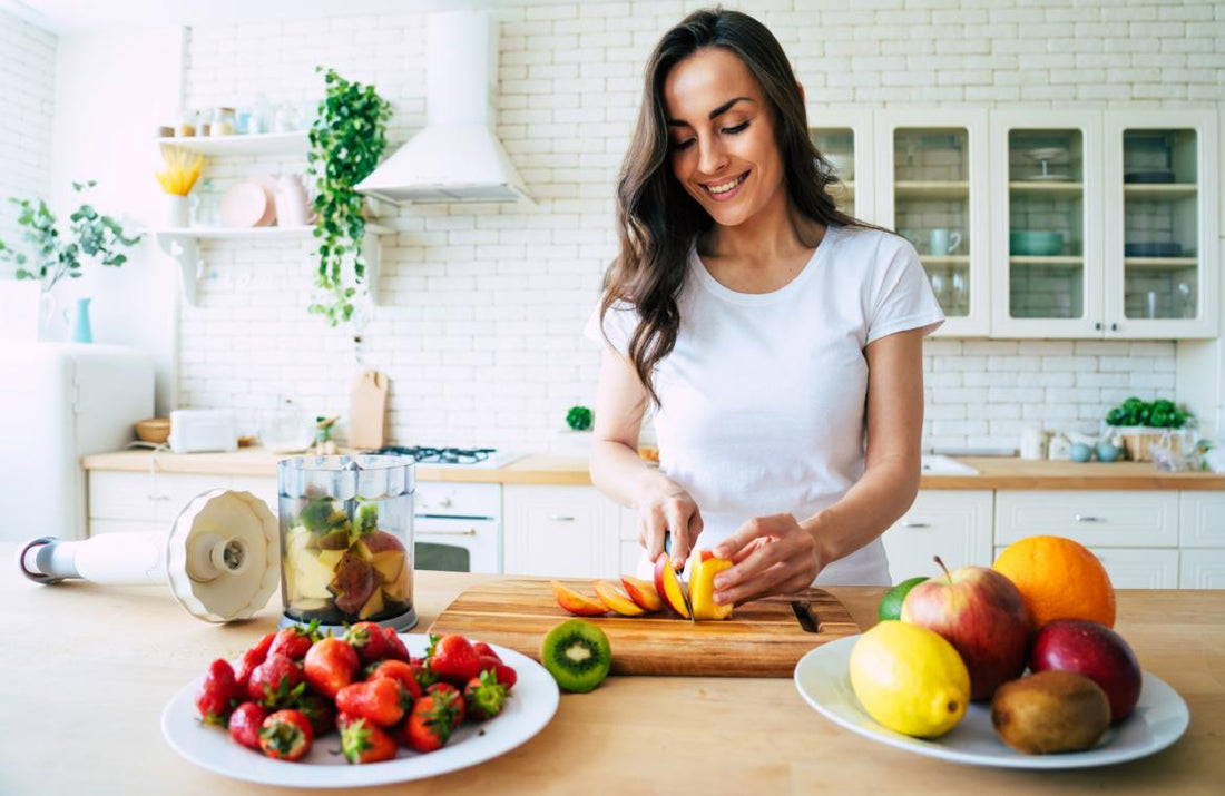 Happy woman in a white t-shirt slicing ingredients for a smoothie at her kitchen counter.