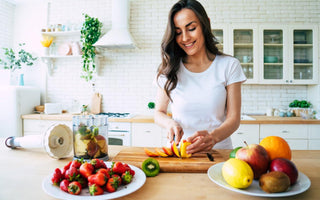 Happy woman in a white t-shirt slicing ingredients for a smoothie at her kitchen counter.