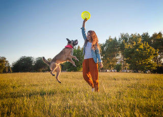 Woman playing frisbee with her dog in an open field.