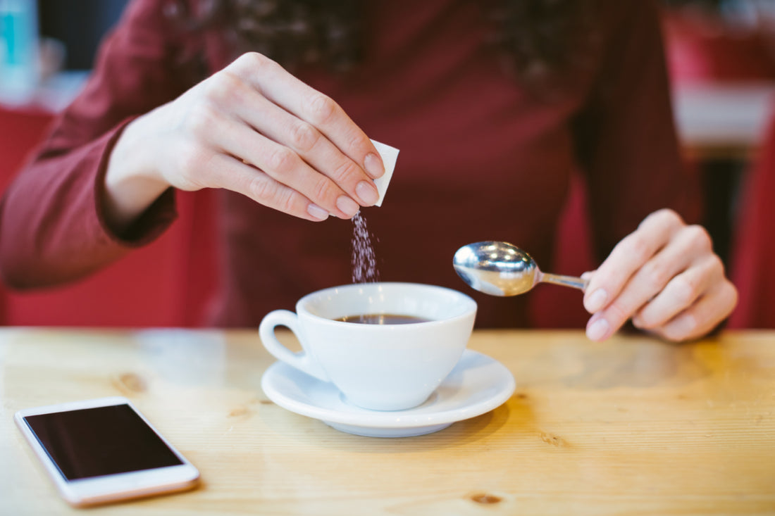 Woman wearing a red long sleeve shirt pouring sweetener out of a small packet into her cup of tea.