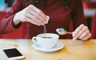 Woman wearing a red long sleeve shirt pouring sweetener out of a small packet into her cup of tea.