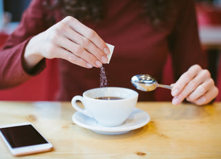 Woman wearing a red long sleeve shirt pouring sweetener out of a small packet into her cup of tea.