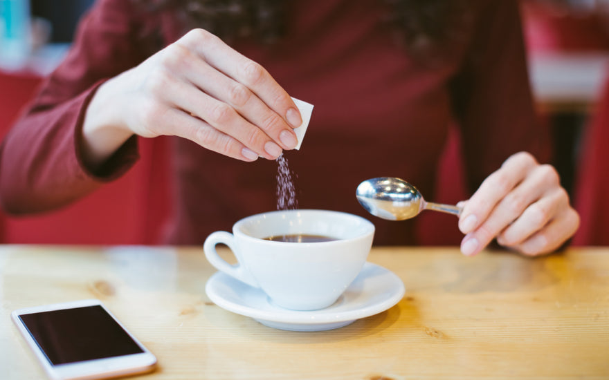 Woman wearing a red long sleeve shirt pouring sweetener out of a small packet into her cup of tea.