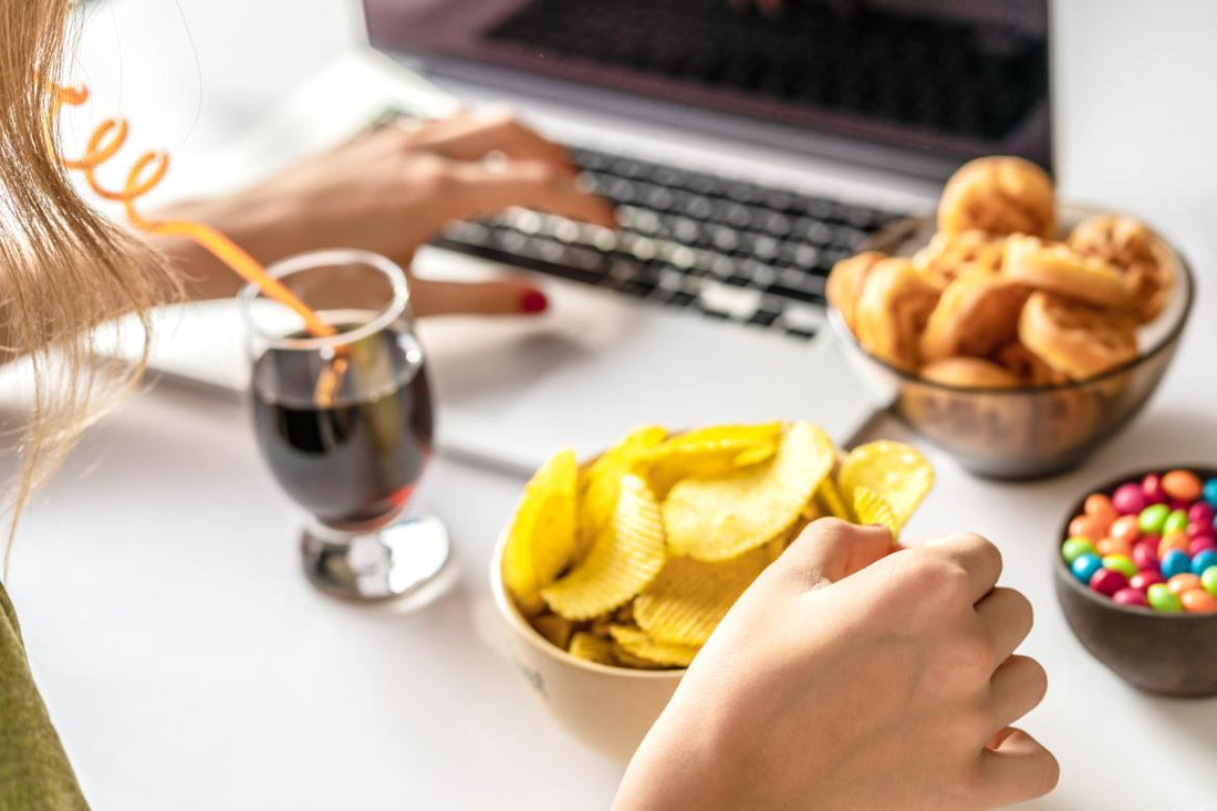 Women sitting in front of her laptop with a glass of soda, a bowl of chips, and other snacks in front of her.