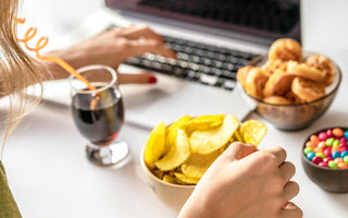 Women sitting in front of her laptop with a glass of soda, a bowl of chips, and other snacks in front of her.