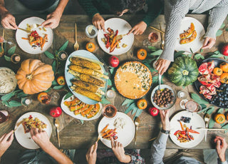 Top down view of a holiday dinner table as people reach to serve themselves food.