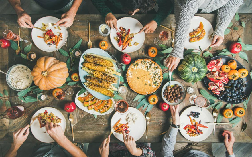 Top down view of a holiday dinner table as people reach to serve themselves food.