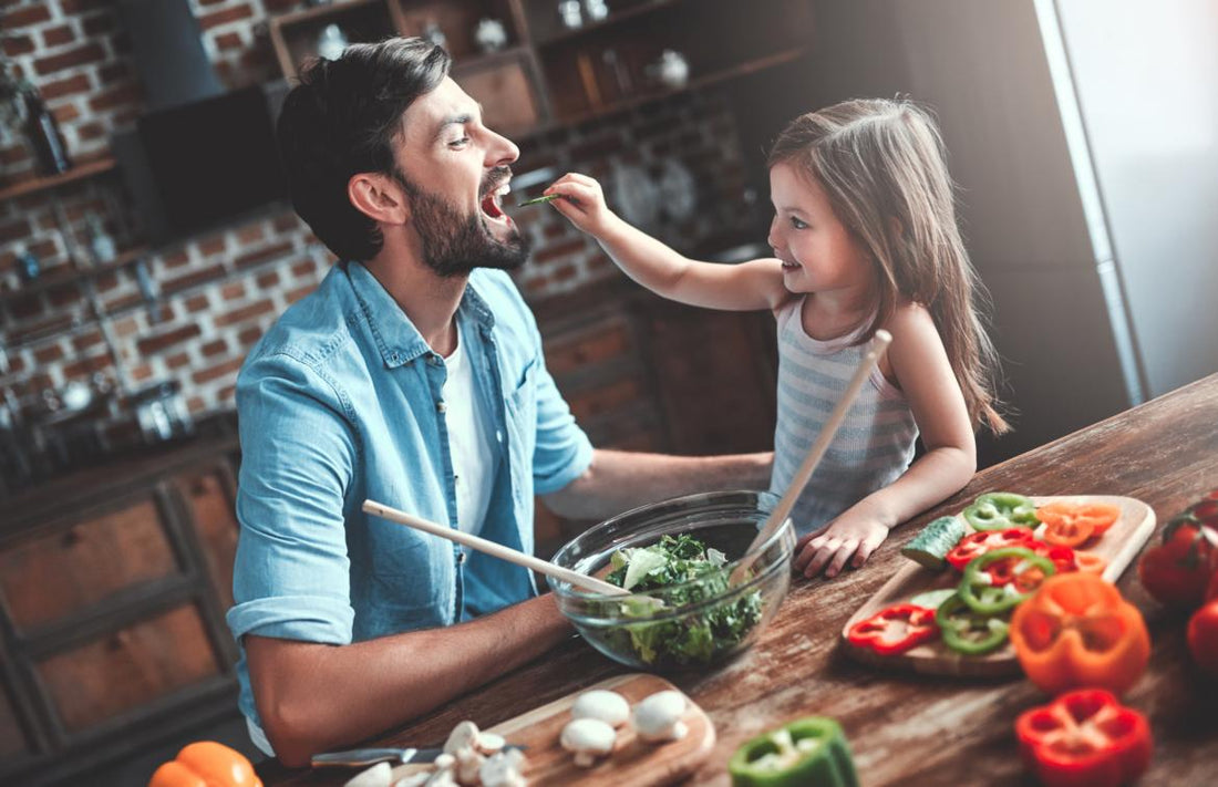 Young girl feeding her dad a piece of a green vegetable at the dinner table. 