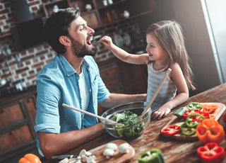 Young girl feeding her dad a piece of a green vegetable at the dinner table. 