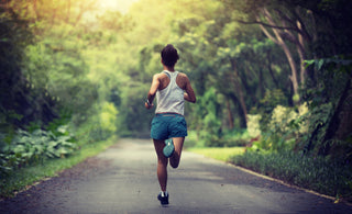 Young adult female in a white tank top and blue shorts running down a train through the woods.