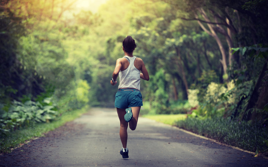 Young adult female in a white tank top and blue shorts running down a train through the woods.