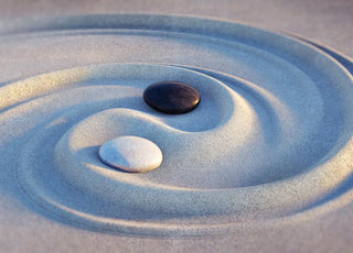 Two pebbles, one black and one white, sitting in the middle of a swirl drawn in the sand. 