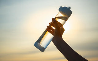 Female hand holding a clear water bottle full of water up in the air at sunset. 