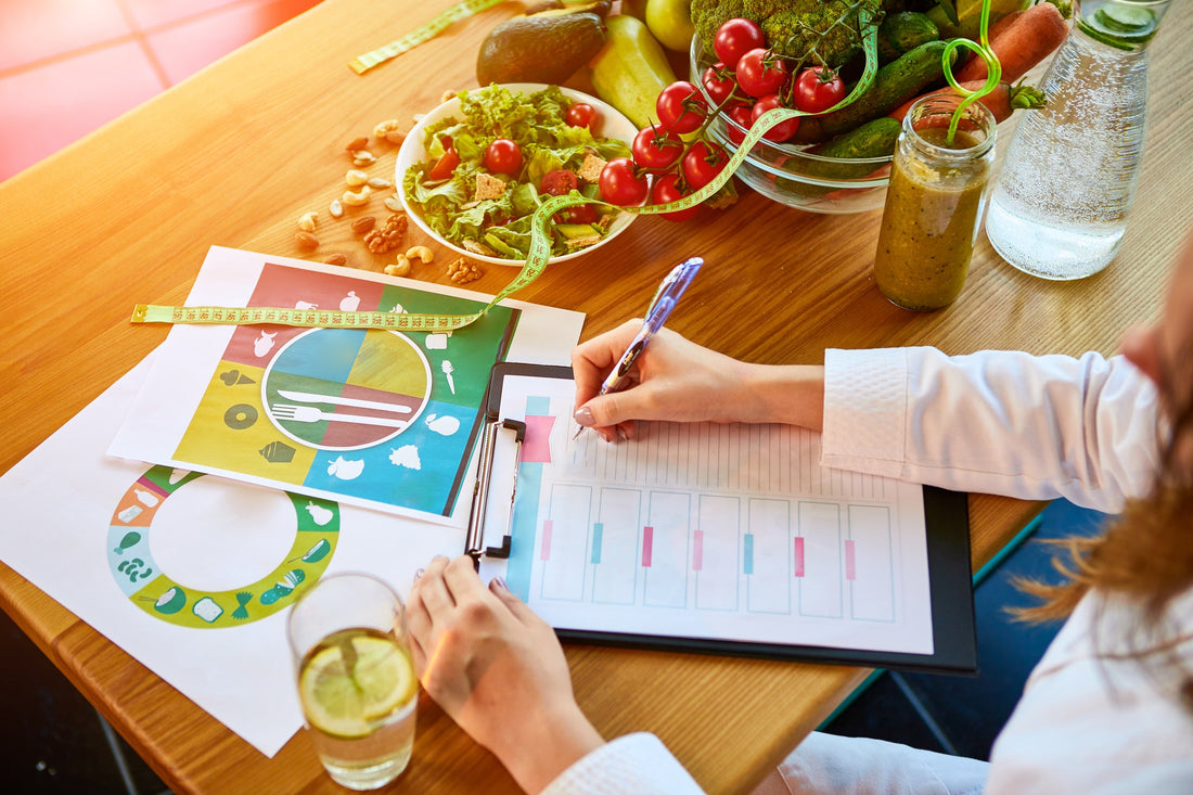 Woman sitting at a table with different healthy ingredients across it while she writes an eating plan.