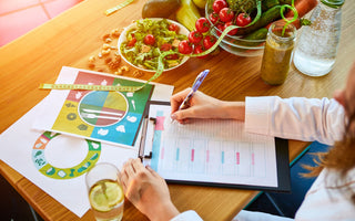 Woman sitting at a table with different healthy ingredients across it while she writes an eating plan.