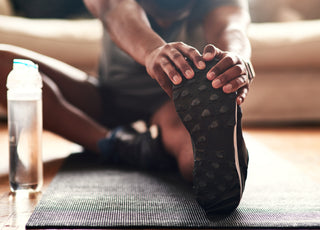 Man sitting on a black yoga matt with one leg out in front of him as he stretches.