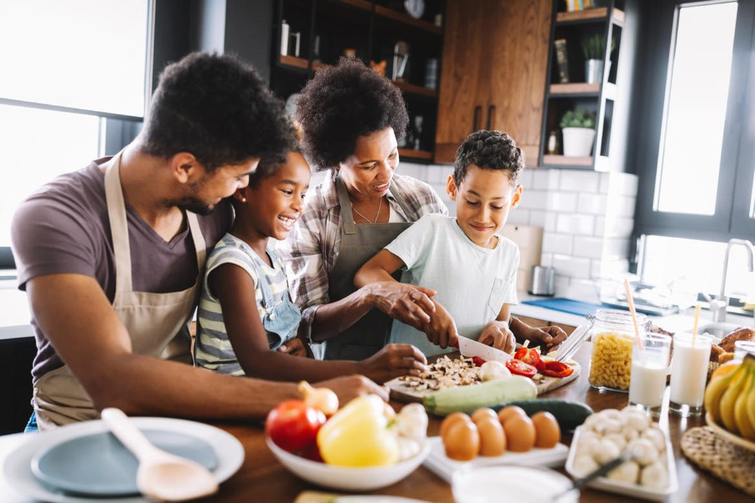Family of four grouped around a cutting board with the youngest child chopping mushrooms while they cook dinner together.