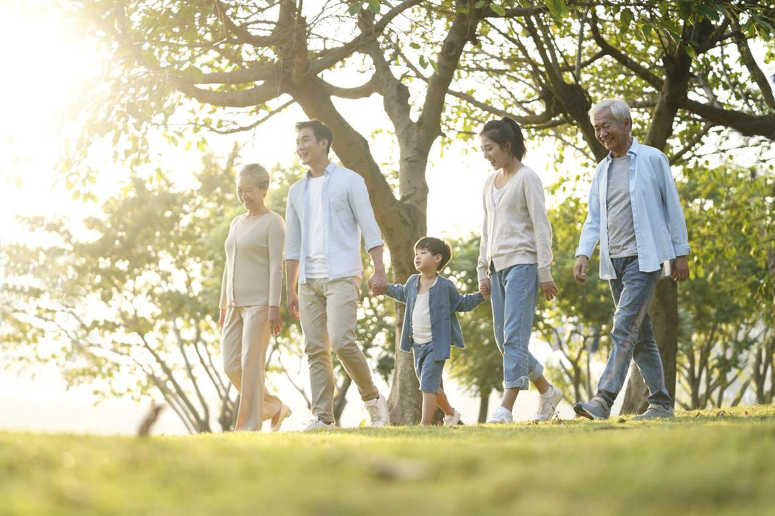 Multi-generational family holding hands and walking through a park.