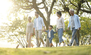 Multi-generational family holding hands and walking through a park.