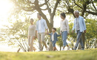 Multi-generational family holding hands and walking through a park.