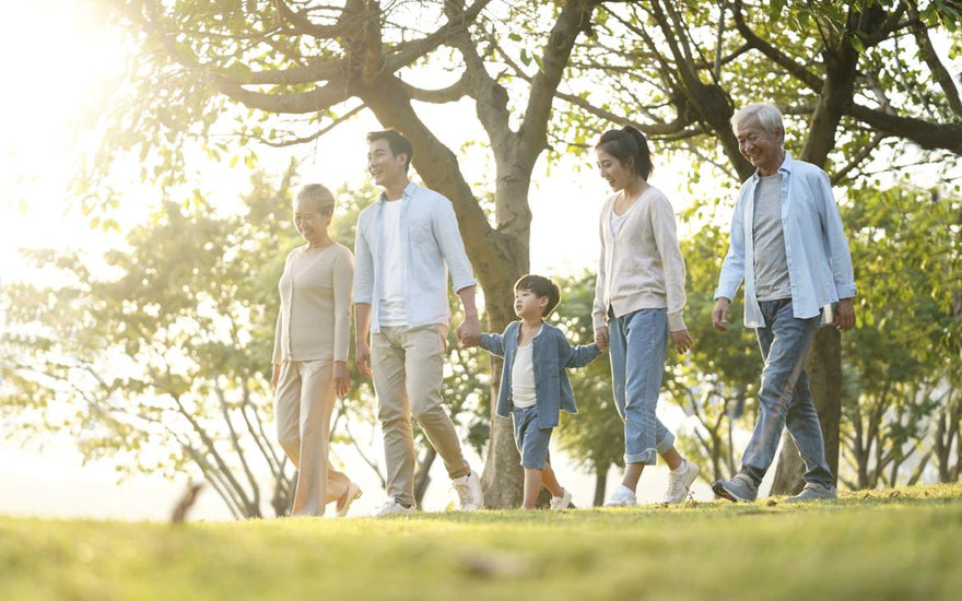 Multi-generational family holding hands and walking through a park.