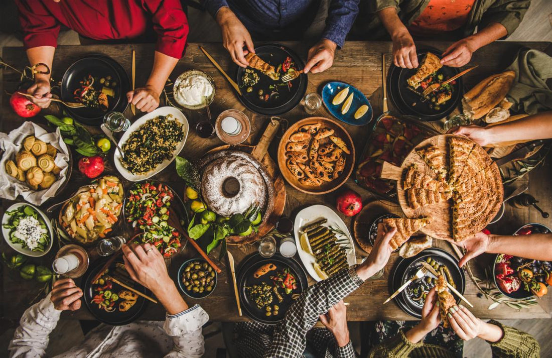 Birds-eye view of a wooden table full of common holiday foods as people reach toward items to serve themselves.