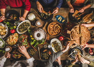 Birds-eye view of a wooden table full of common holiday foods as people reach toward items to serve themselves.