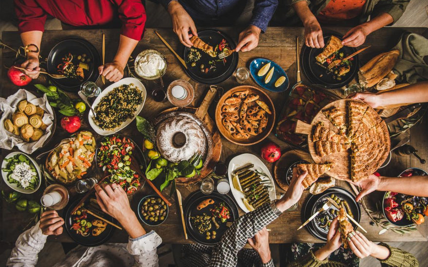 Birds-eye view of a wooden table full of common holiday foods as people reach toward items to serve themselves.