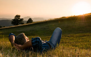 Older adult man laying in a grassy field watching the sunset. 