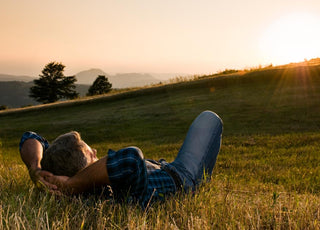 Older adult man laying in a grassy field watching the sunset. 