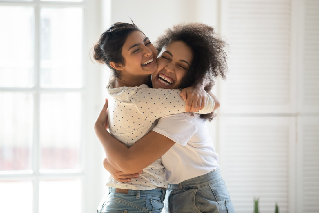 Two young adult females smiling and hugging. 