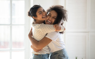 Two young adult females smiling and hugging. 