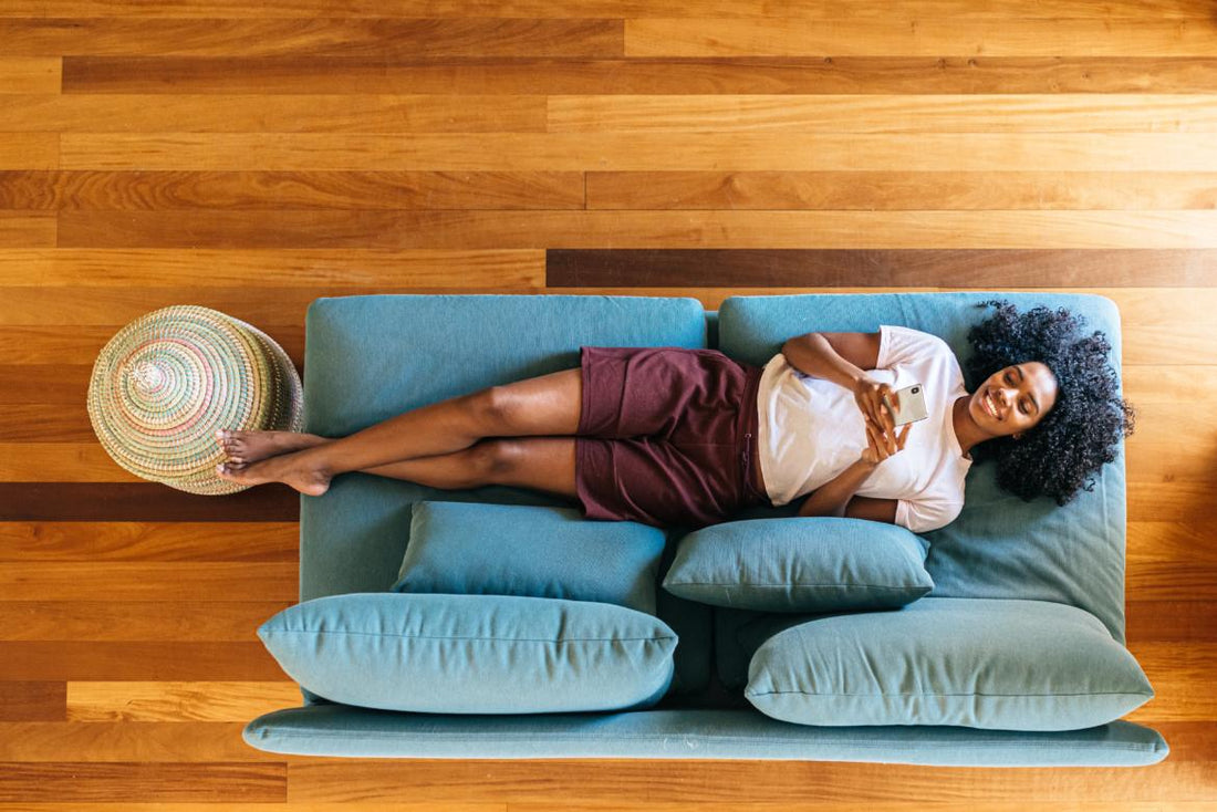 Top down view of a woman laying on a blue couch, relaxing while looking at her phone. 