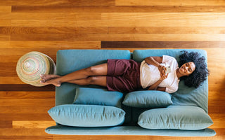 Top down view of a woman laying on a blue couch, relaxing while looking at her phone. 