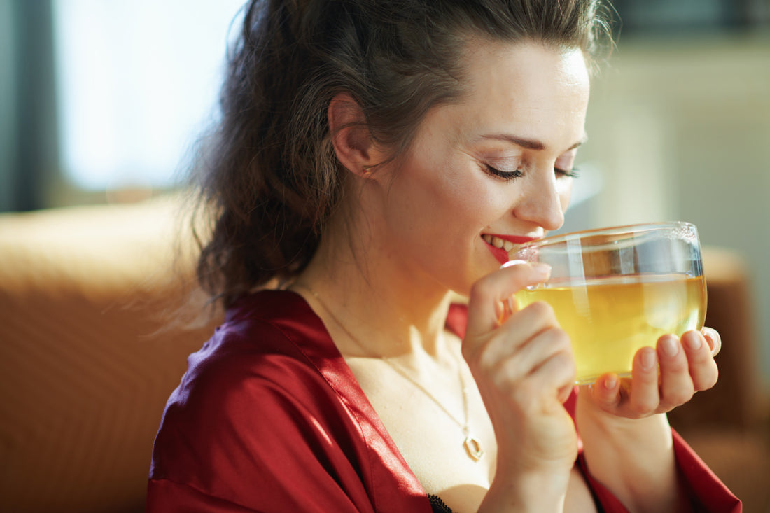 Happy woman in a red shirt drinking herbal tea from a clear mug. 