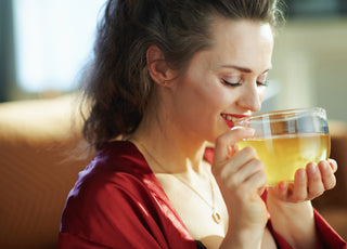 Happy woman in a red shirt drinking herbal tea from a clear mug. 