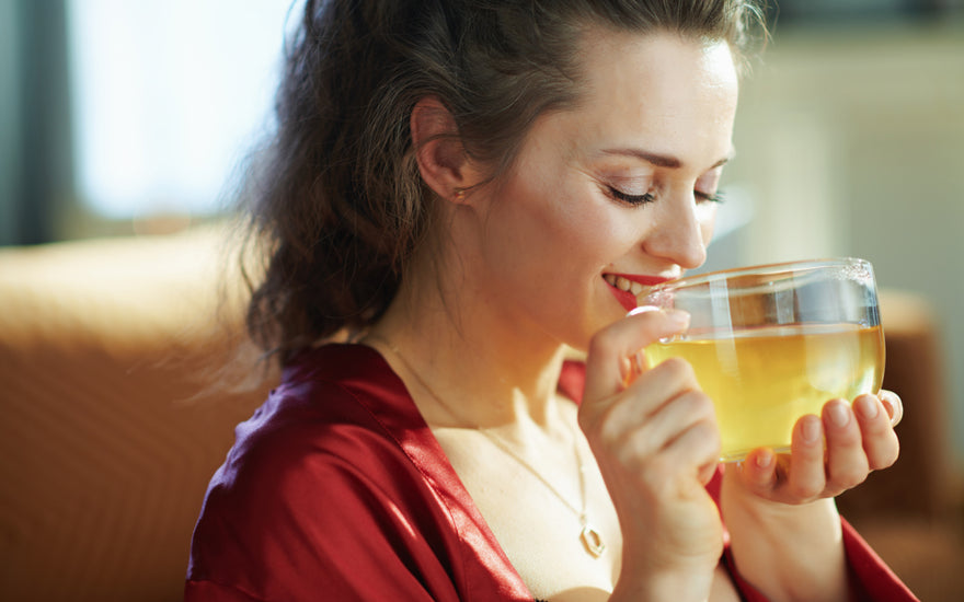 Happy woman in a red shirt drinking herbal tea from a clear mug. 