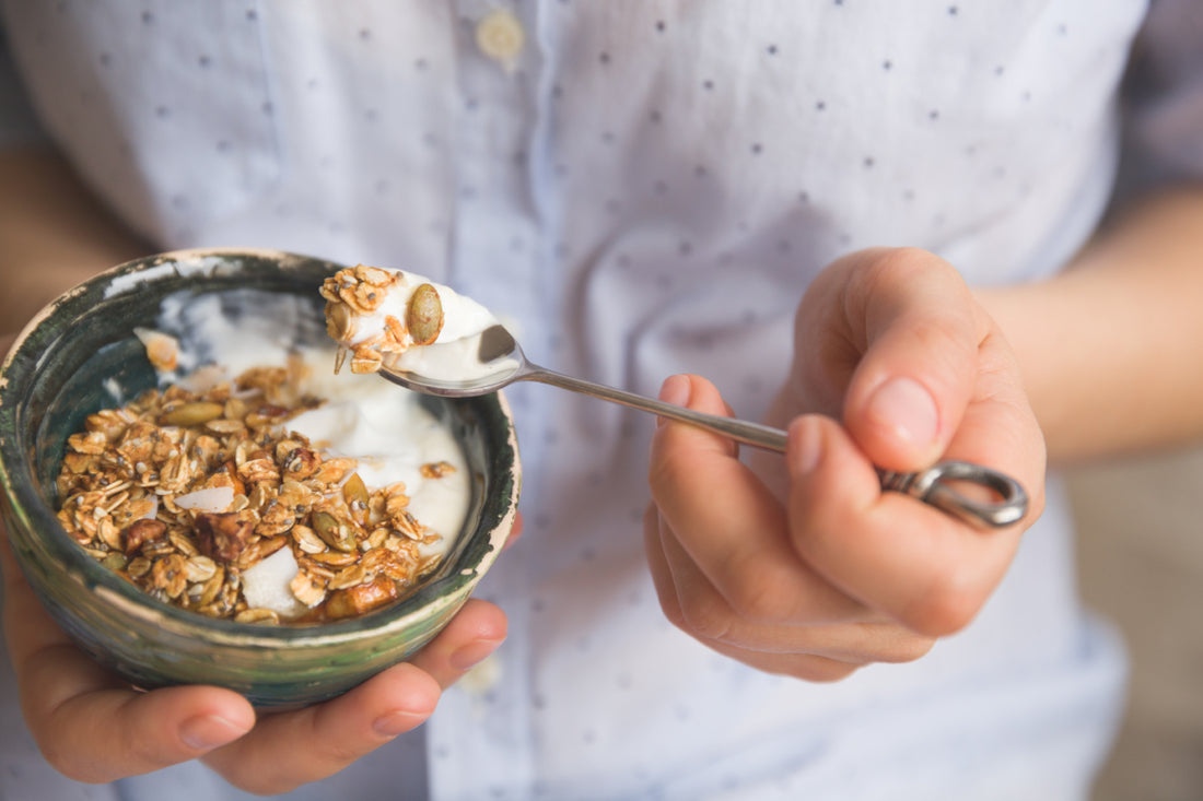 Close up of a person holding a small stone bowl of yogurt topped with granola.