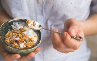 Close up of a person holding a small stone bowl of yogurt topped with granola.