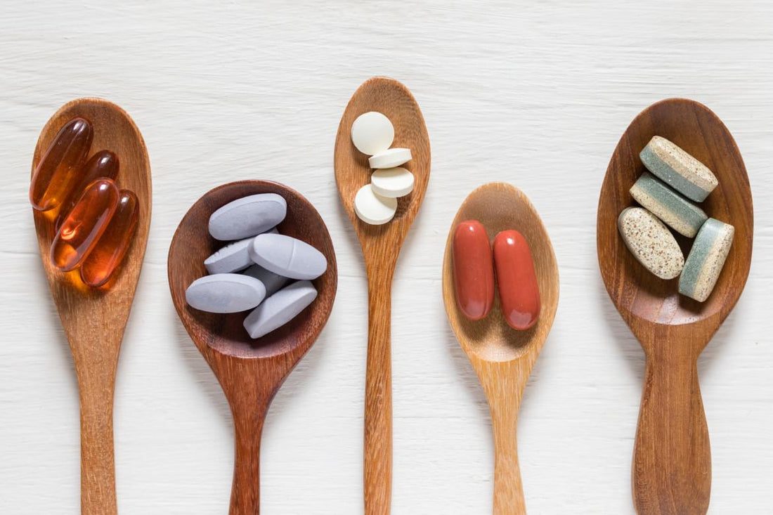 Five wooden spoons of various sizes each holding a two to five of a different type of pill.