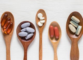 Five wooden spoons of various sizes each holding a two to five of a different type of pill.