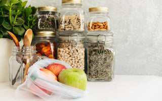 A white counter top with fresh apples in a plastic bag and glass jars filled with pantry staples sitting on top of it.