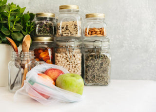 A white counter top with fresh apples in a plastic bag and glass jars filled with pantry staples sitting on top of it.