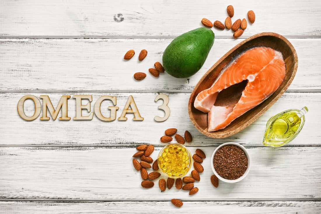 Wooden letters spelling "OMEGA 3" laying on a wooden table surrounded by fatty foods like salmon and avocado.