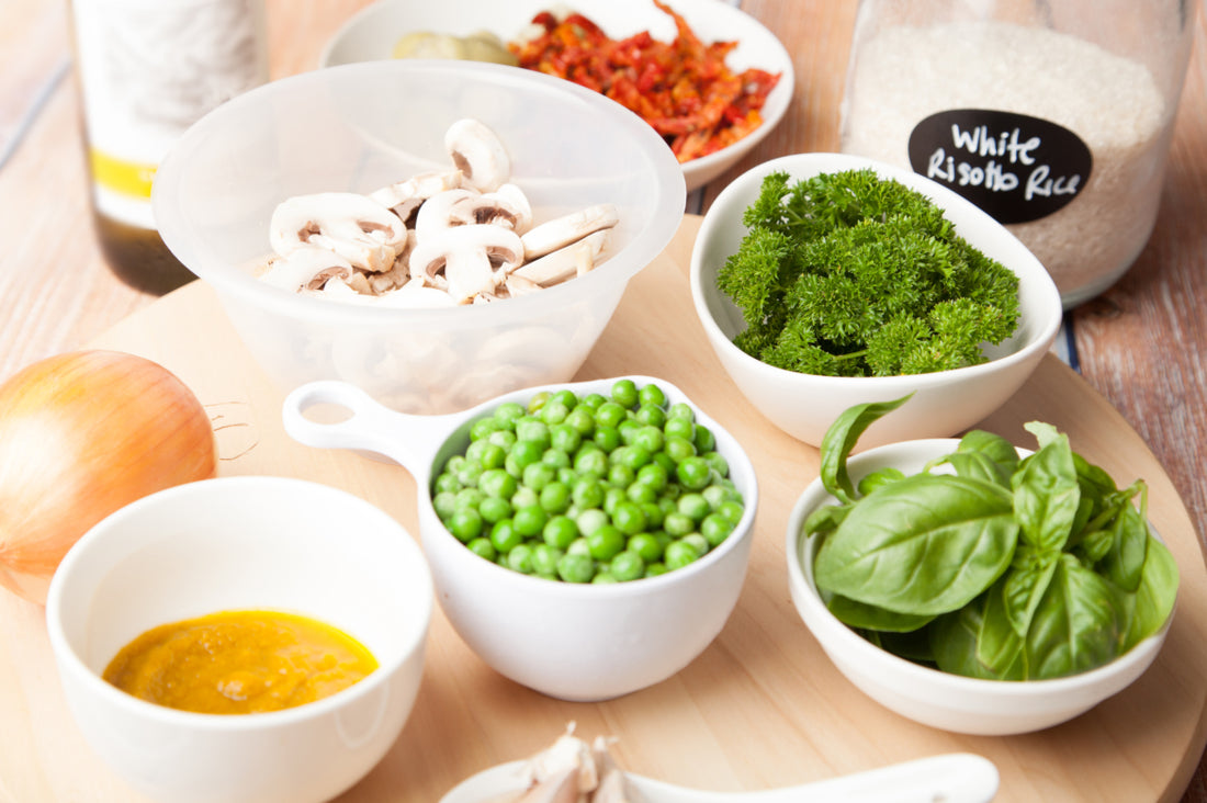 Table full of bowl with whole foods like mushrooms, broccoli, and peas.