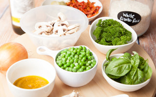 Table full of bowl with whole foods like mushrooms, broccoli, and peas.