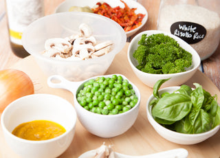 Table full of bowl with whole foods like mushrooms, broccoli, and peas.