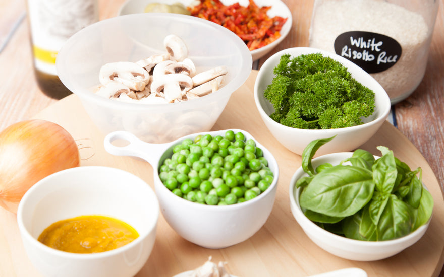 Table full of bowl with whole foods like mushrooms, broccoli, and peas.