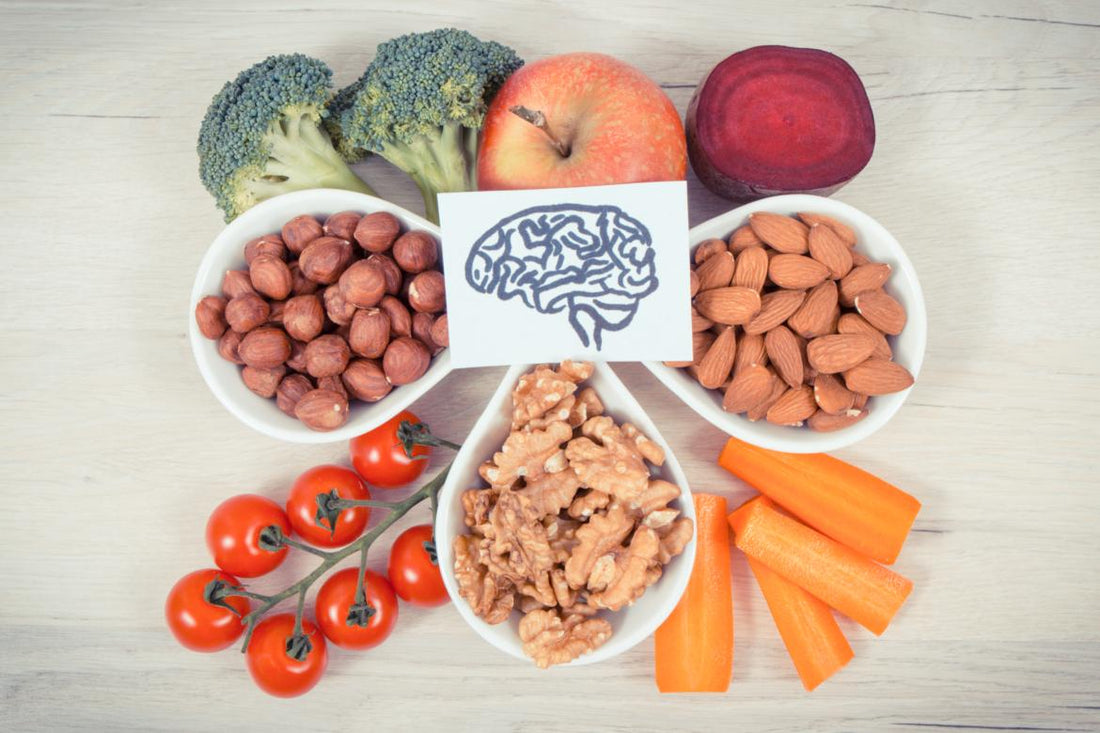 A piece of paper with a drawing of a brain on it sitting on top of an array of healthy foods including apples, broccoli, bowls of nuts, tomoatos, and peppers.